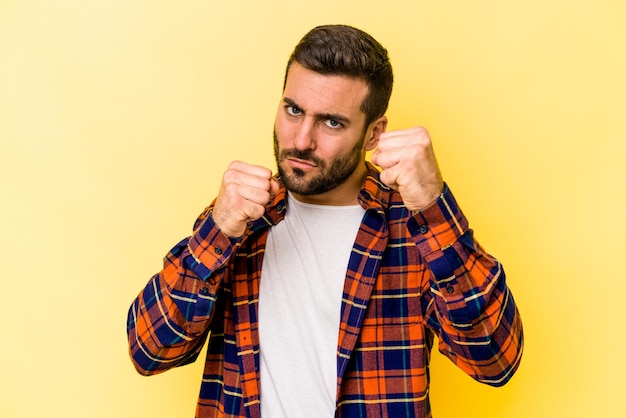 Young caucasian man isolated on yellow background throwing a punch anger fighting due to an argument boxing