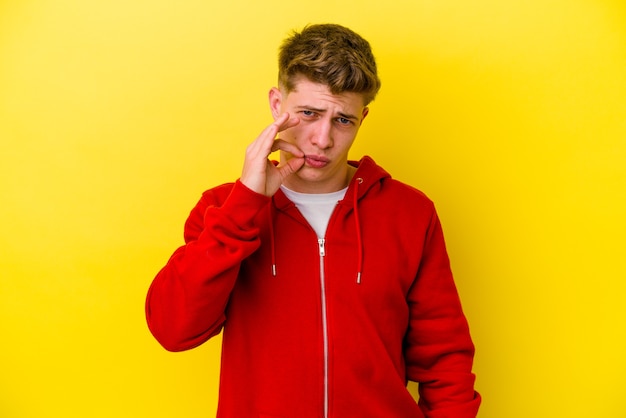 Young caucasian man isolated on yellow background with fingers on lips keeping a secret.