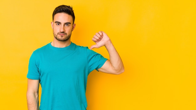 Young caucasian man isolated on yellow bakground showing a dislike gesture, thumbs down. Disagreement concept.