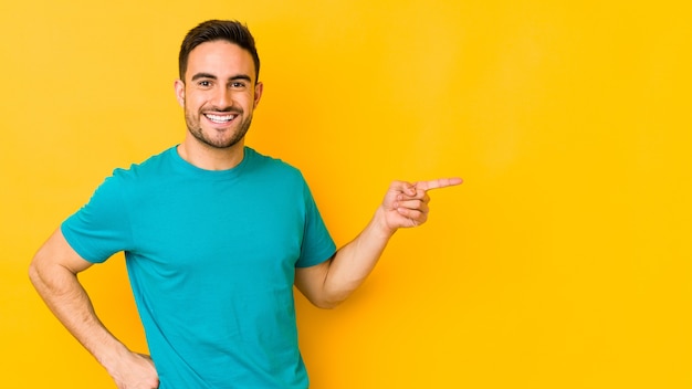 Young caucasian man isolated on yellow bakground smiling cheerfully pointing with forefinger away.