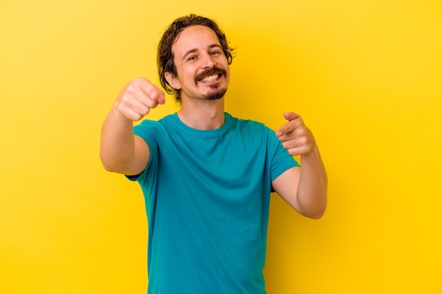 Young caucasian man isolated on yellow wall cheerful smiles pointing to front