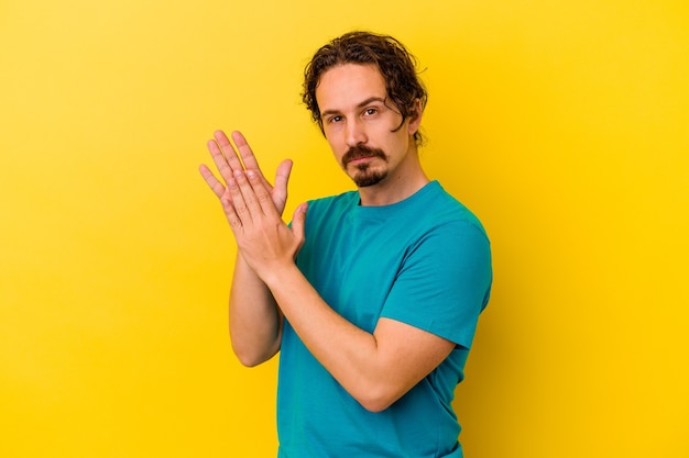 Young caucasian man isolated on yellow wall feeling energetic and comfortable, rubbing hands confident