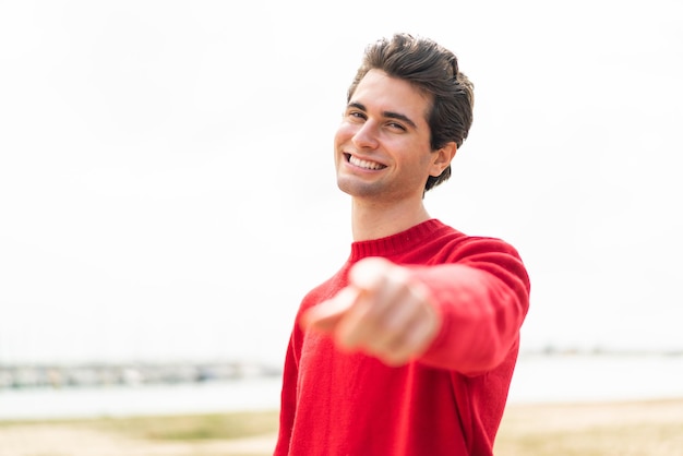 Young caucasian man man holding a shopping basket full of food isolated on red background giving a thumbs up gesture