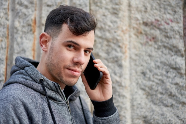 Young caucasian man multitasking on the street leaning against a wall and chatting on his phone