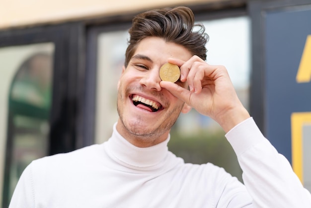 Young caucasian man at outdoors holding a Bitcoin with happy expression