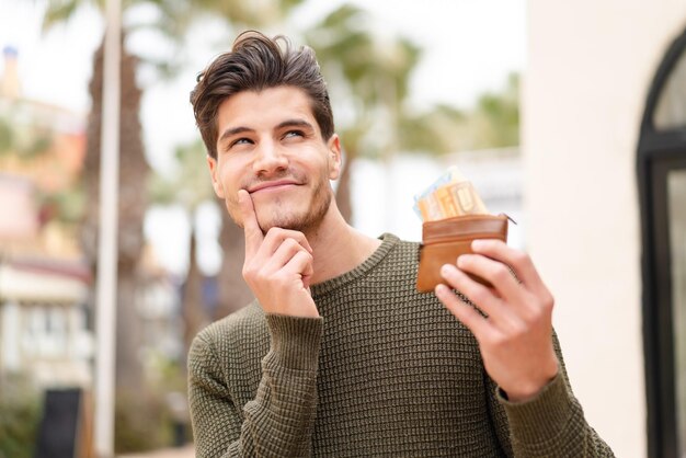 Young caucasian man at outdoors holding wallet with money