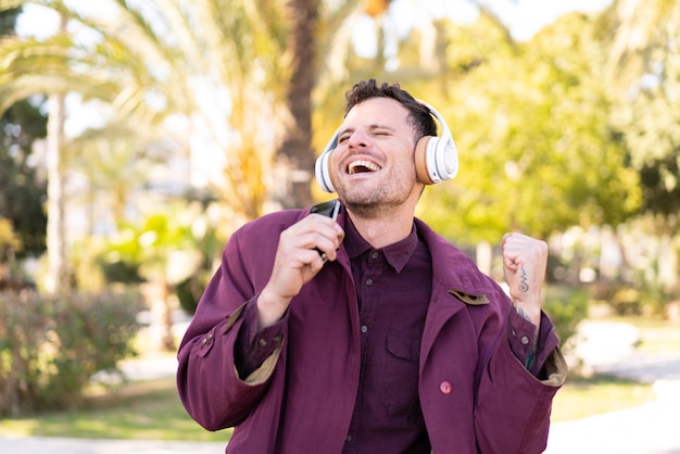 Young caucasian man at outdoors listening music with a mobile and singing