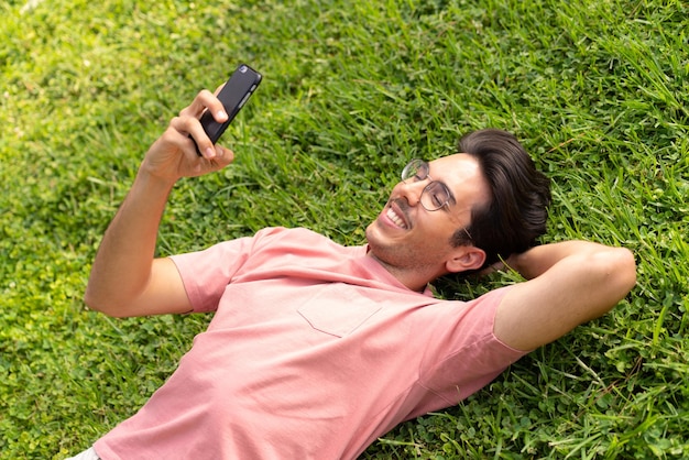 Young caucasian man at outdoors in a park using mobile phone with happy expression