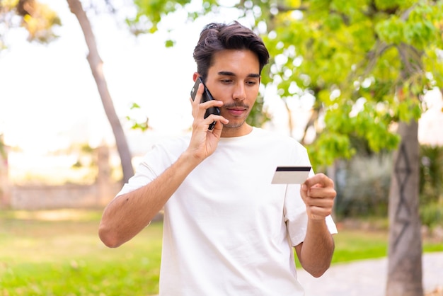 Young caucasian man in a park buying with the mobile with a credit card