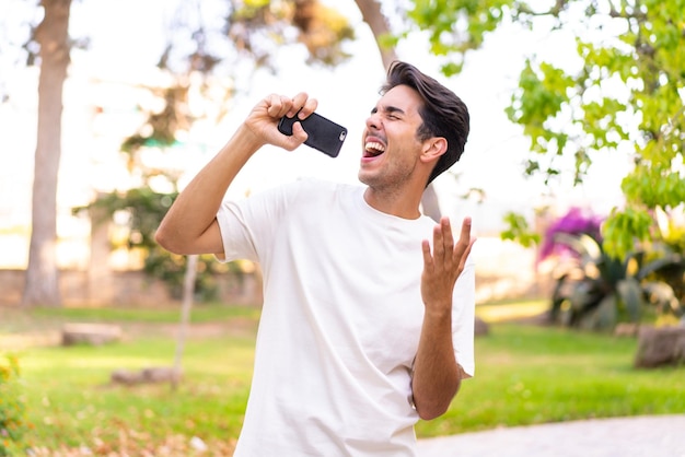 Young caucasian man in a park using mobile phone and singing