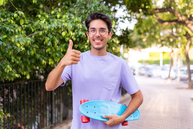 Young caucasian man in a park with a skate and pointing to the side