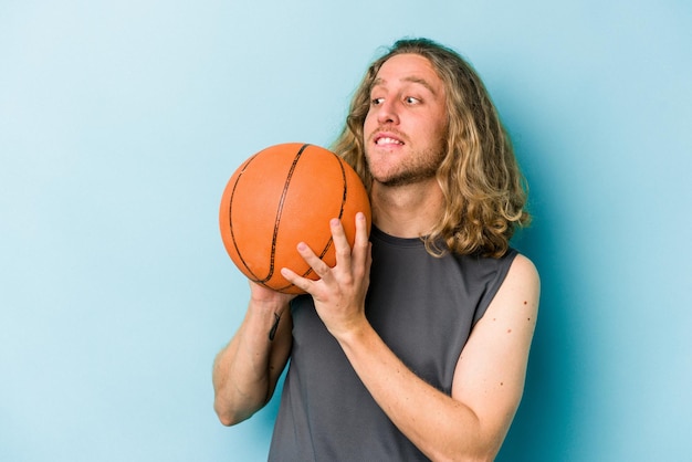 Young caucasian man playing basketball isolated on blue background