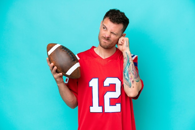 Young caucasian man playing rugby isolated on blue background frustrated and covering ears