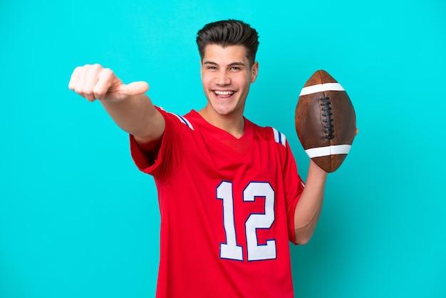 Young Caucasian man Playing rugby isolated on blue background giving a thumbs up gesture