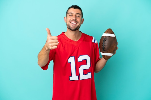 Young caucasian man playing rugby isolated on blue background with thumbs up because something good has happened