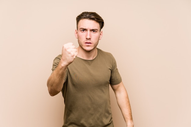 Young caucasian man posing isolated showing fist to camera, aggressive facial expression.