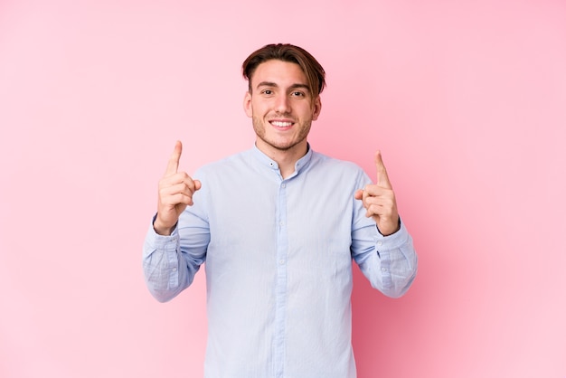 Young caucasian man posing on pink isolated indicates with both fore fingers up showing a blank space.