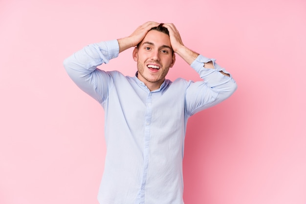 Young caucasian man posing in a pink isolated laughs joyfully keeping hands on head. Happiness concept.