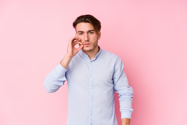 Young caucasian man posing in a pink wall isolated with fingers on lips keeping a secret.