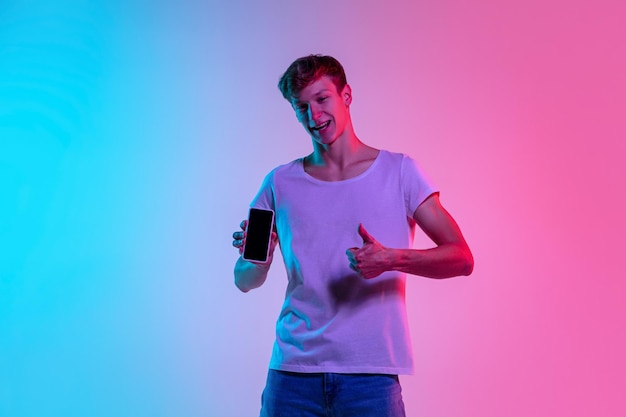 Young caucasian man's jumping high on gradient blue-pink studio background in neon light