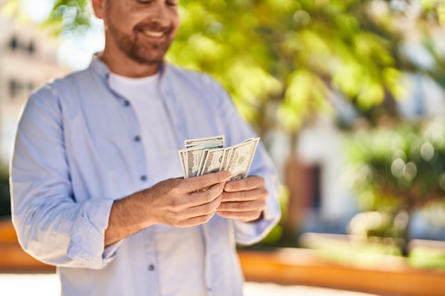 Young caucasian man smiling confident counting dollars at park