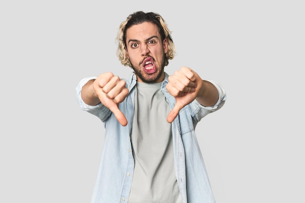 Young Caucasian man in studio setting showing thumb down and expressing dislike