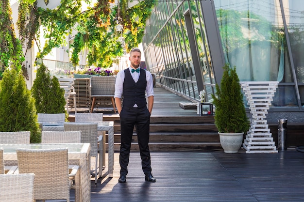 Young caucasian man in a suit with a bow tie in a summer street cafe