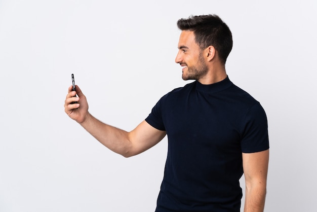 Young caucasian man using mobile phone isolated on white background with happy expression