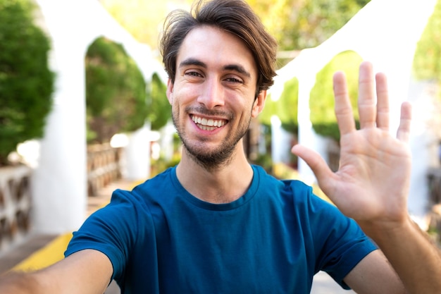 Young caucasian man wave hello on a video call Male take selfie in city park