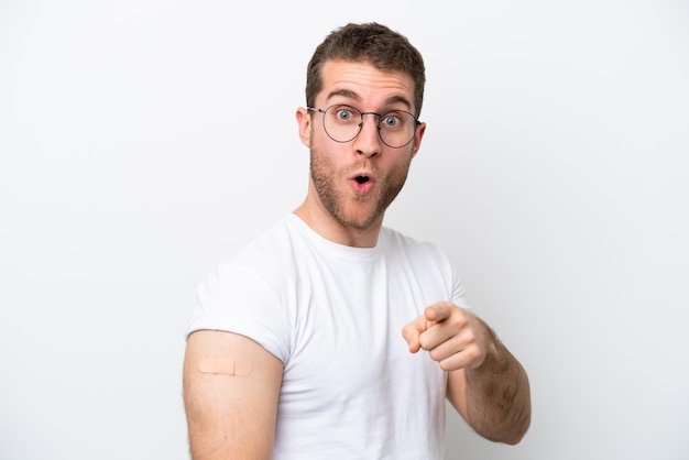 Young caucasian man wearing band aids isolated on white background surprised and pointing front