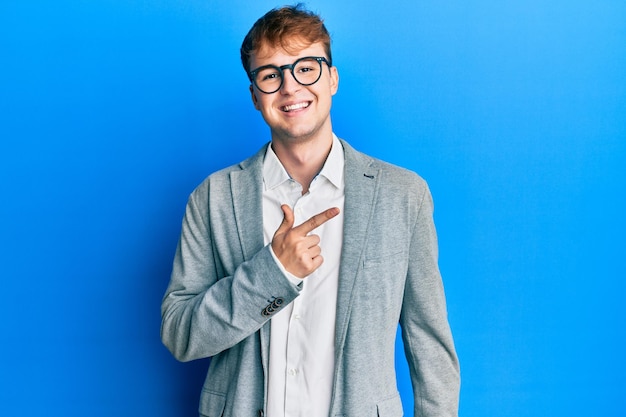 Young caucasian man wearing elegant clothes and glasses cheerful with a smile of face pointing with hand and finger up to the side with happy and natural expression on face