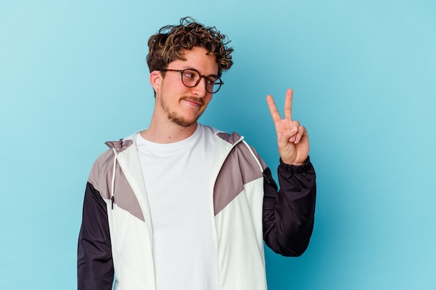 Young caucasian man wearing eyeglasses isolated on blue background joyful and carefree showing a peace symbol with fingers.