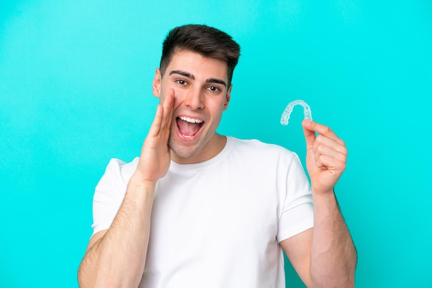 Young caucasian man wearing holding invisible braces isolated on blue background shouting with mouth wide open