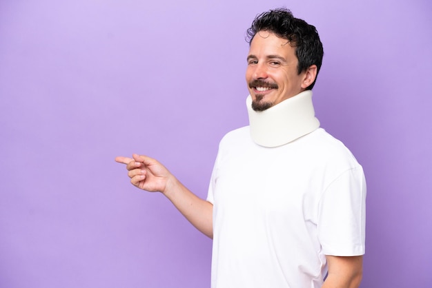 Young caucasian man wearing neck brace isolated on purple background pointing finger to the side