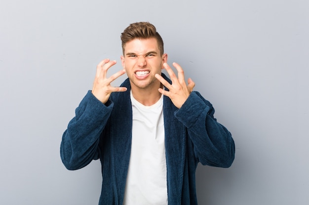 Young caucasian man wearing pajama upset screaming with tense hands.