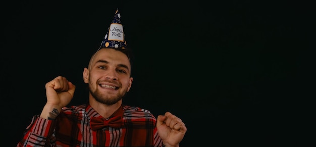 Young Caucasian man wears festive hat with inscription happy party and dances smiling