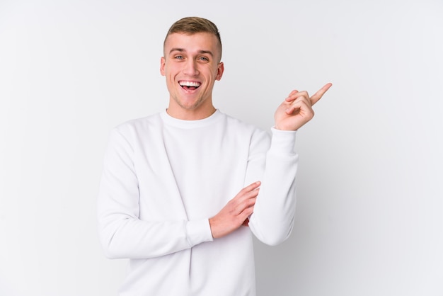 Young caucasian man on white background smiling cheerfully pointing with forefinger away.