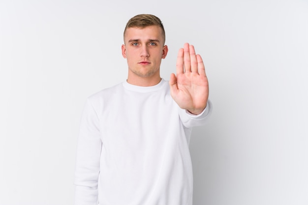 Young caucasian man on white standing with outstretched hand showing stop sign, preventing you.