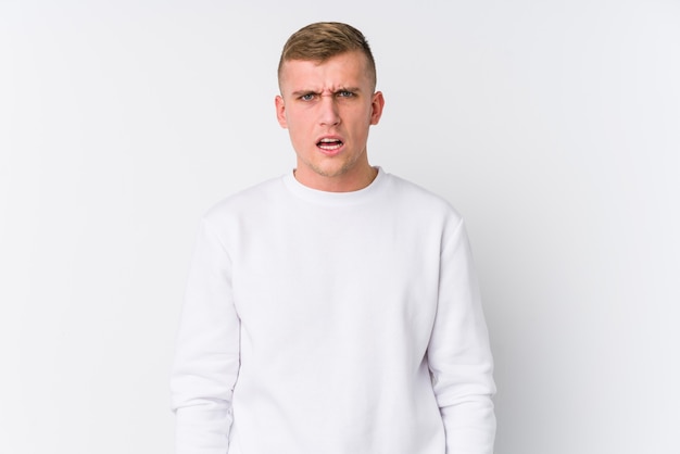 Young caucasian man on white surface screaming very angry and aggressive.