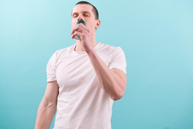 Young caucasian man in a white t-shirt drinking an energy drink with closed eyes on blue background