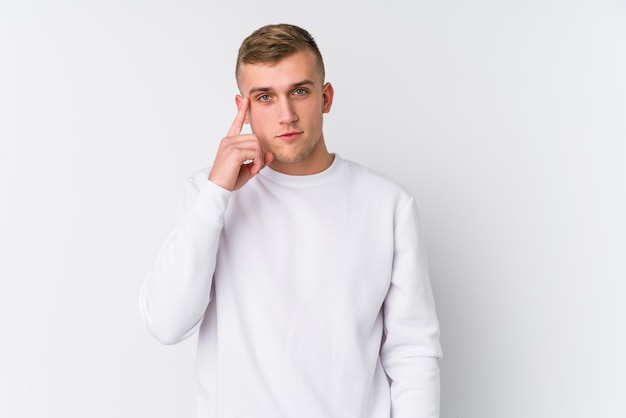 Young caucasian man on white wall pointing temple with finger, thinking, focused on a task.