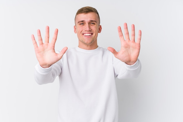 Young caucasian man on white wall showing number ten with hands.