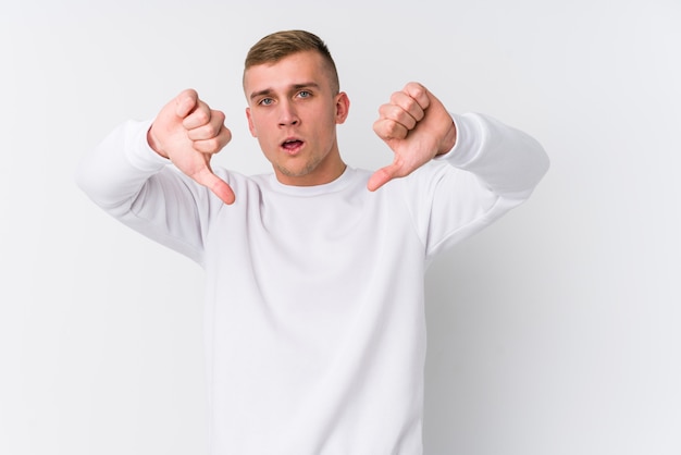 Young caucasian man on white wall showing thumb down and expressing dislike.