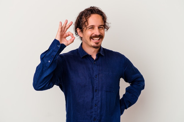 Young caucasian man   winks an eye and holds an okay gesture with hand.