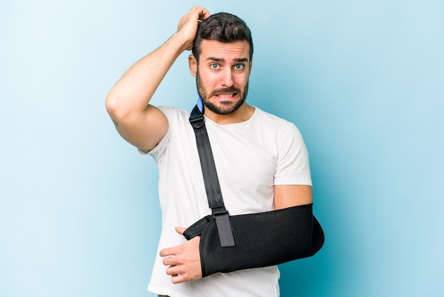 Young caucasian man with broken hand isolated on blue background being shocked she has remembered important meeting