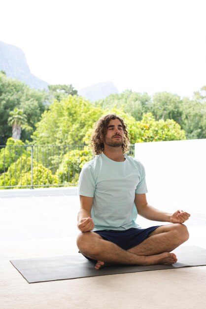 Young Caucasian man with curly hair meditates in a lotus position outdoors