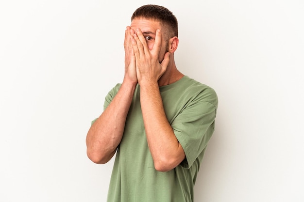 Young caucasian man with diastema isolated on white background blink through fingers frightened and nervous.