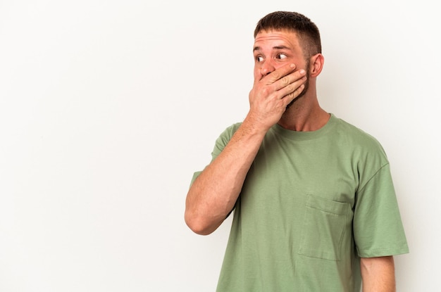 Young caucasian man with diastema isolated on white background thoughtful looking to a copy space covering mouth with hand.