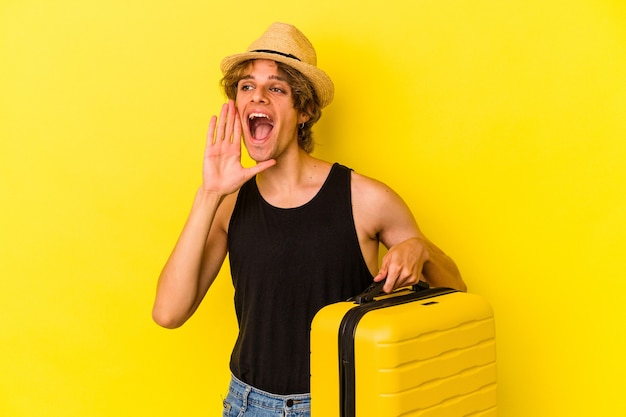 Young caucasian man with makeup going to travel isolated on yellow background  shouting and holding palm near opened mouth.