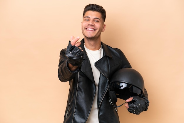 Young caucasian man with a motorcycle helmet isolated on beige background making money gesture